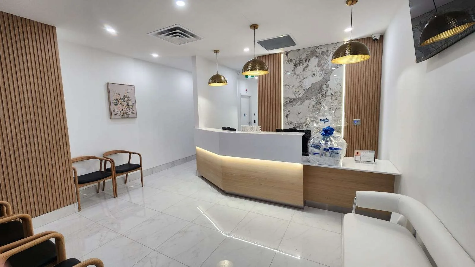 The bright reception and waiting area at Janood Dental in Etobicoke, with a curved front desk and comfortable seating