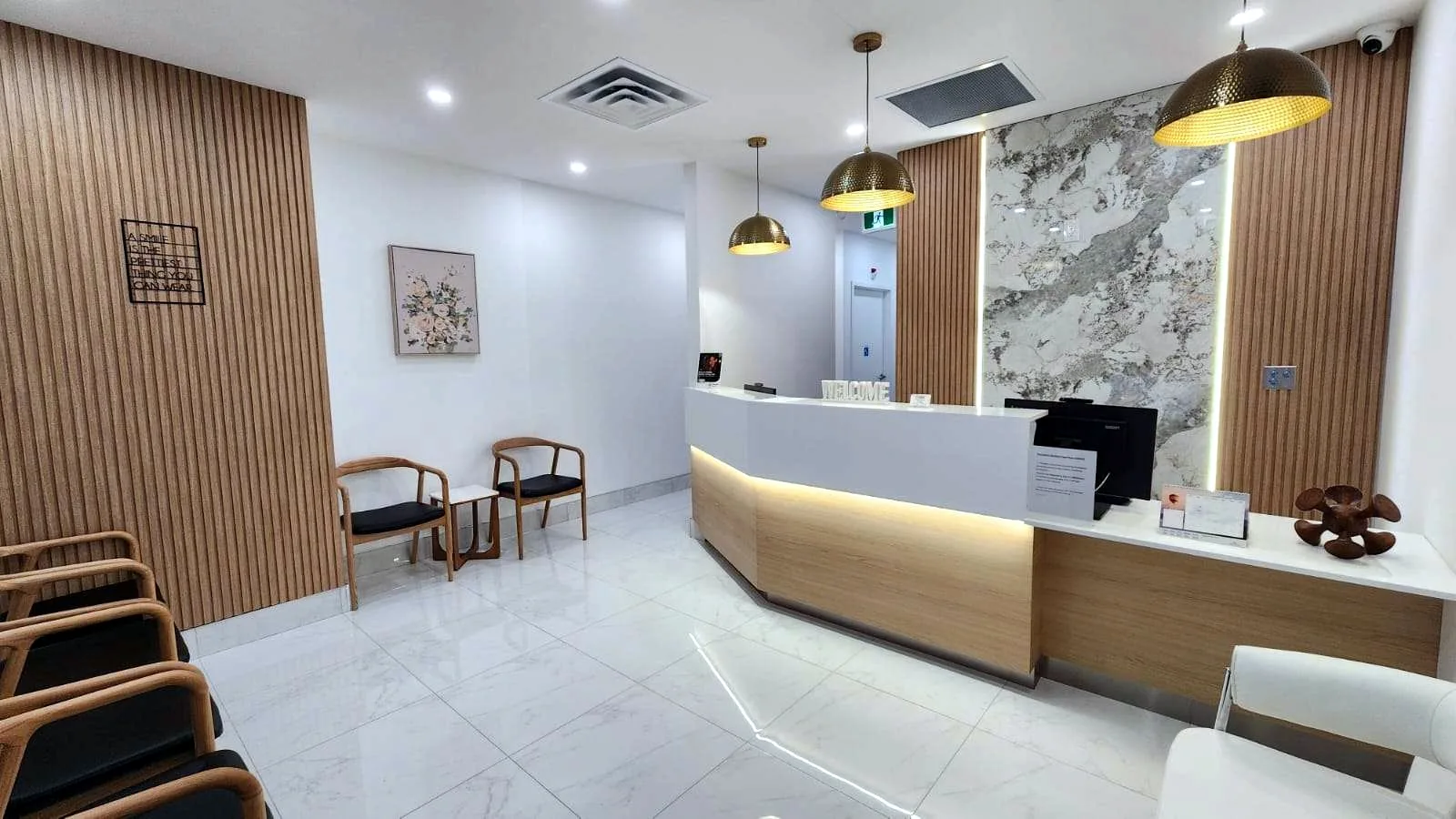 The reception and waiting area at Dr. Janood Dental in Etobicoke, with a curved front desk, wood slat walls, brass pendant lights, and marble floors